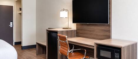 Una habitación de hotel con escritorio, silla, televisión y microondas.