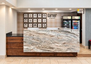 Ein Hotelrezeptionsschalter mit Marmortisch, gerahmte Kunstwerke an der Wand und ein Schild für ein Garnier Geschäft.