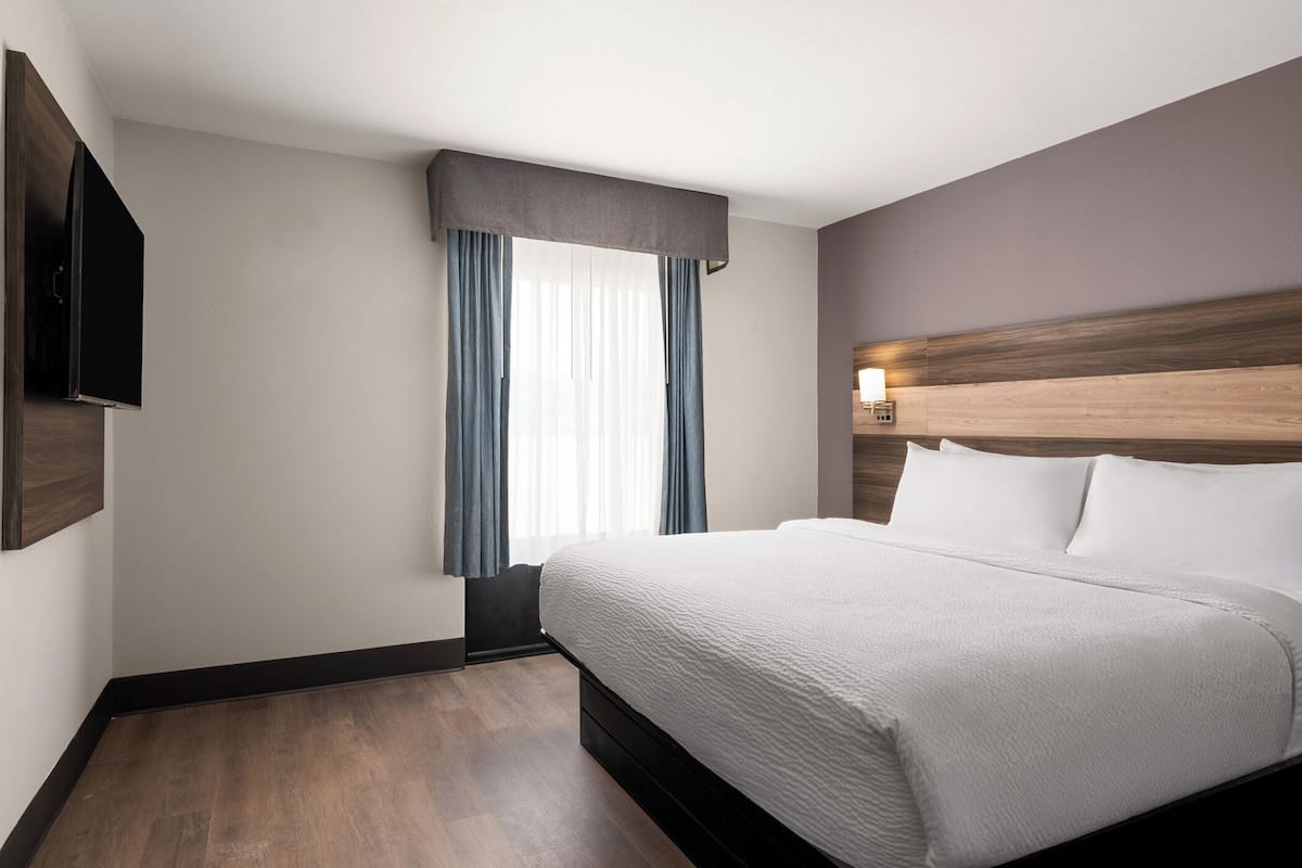 Habitación de hotel con una cama grande, un televisor de pantalla plana montado en la pared y una ventana con cortinas.