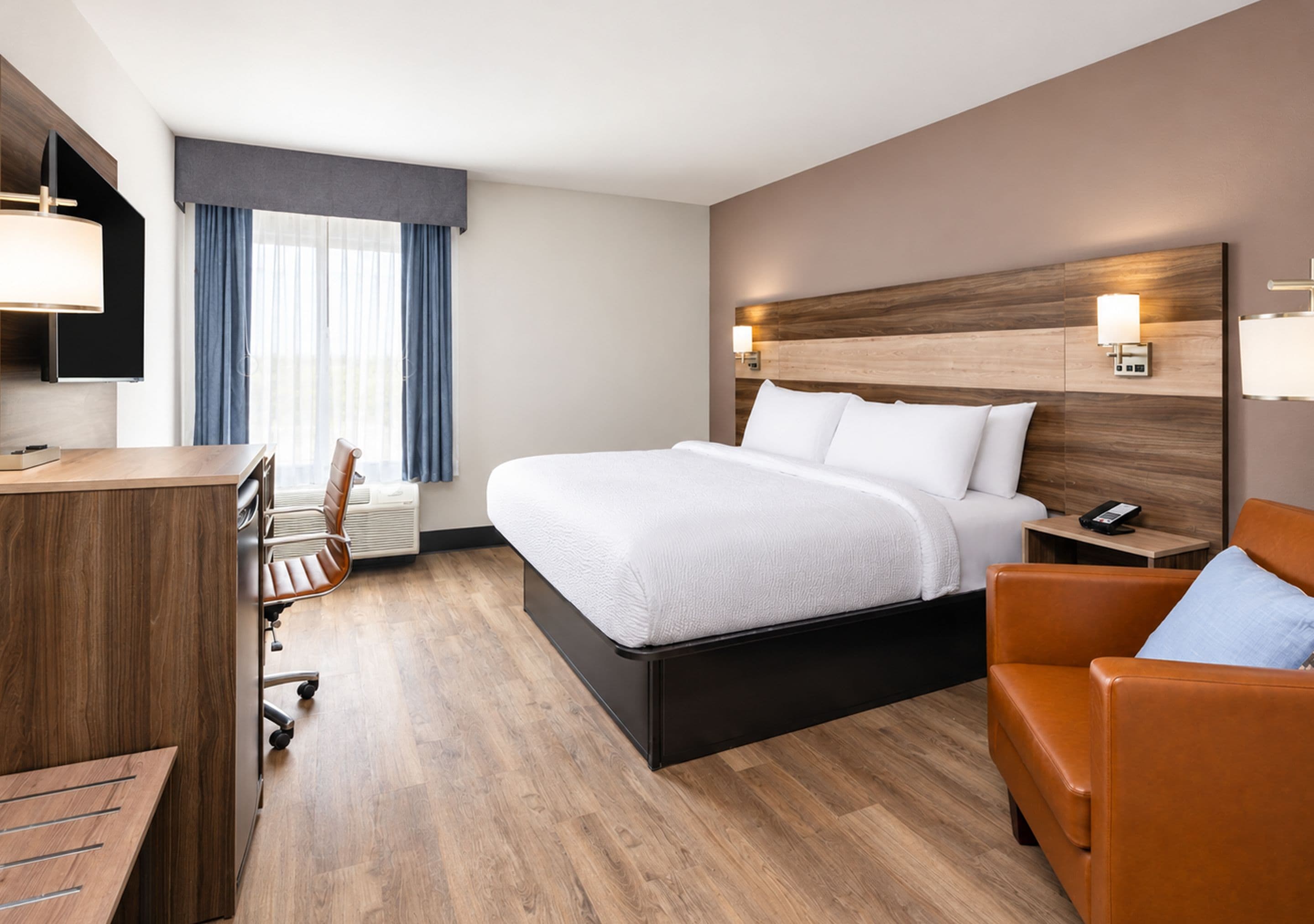 A hotel room with a bed, a desk, a chair, a TV, and a window with curtains.