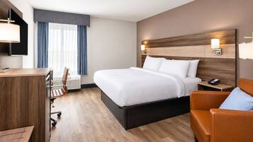 A hotel room with a bed, a desk, a chair, a TV, and a window with curtains.