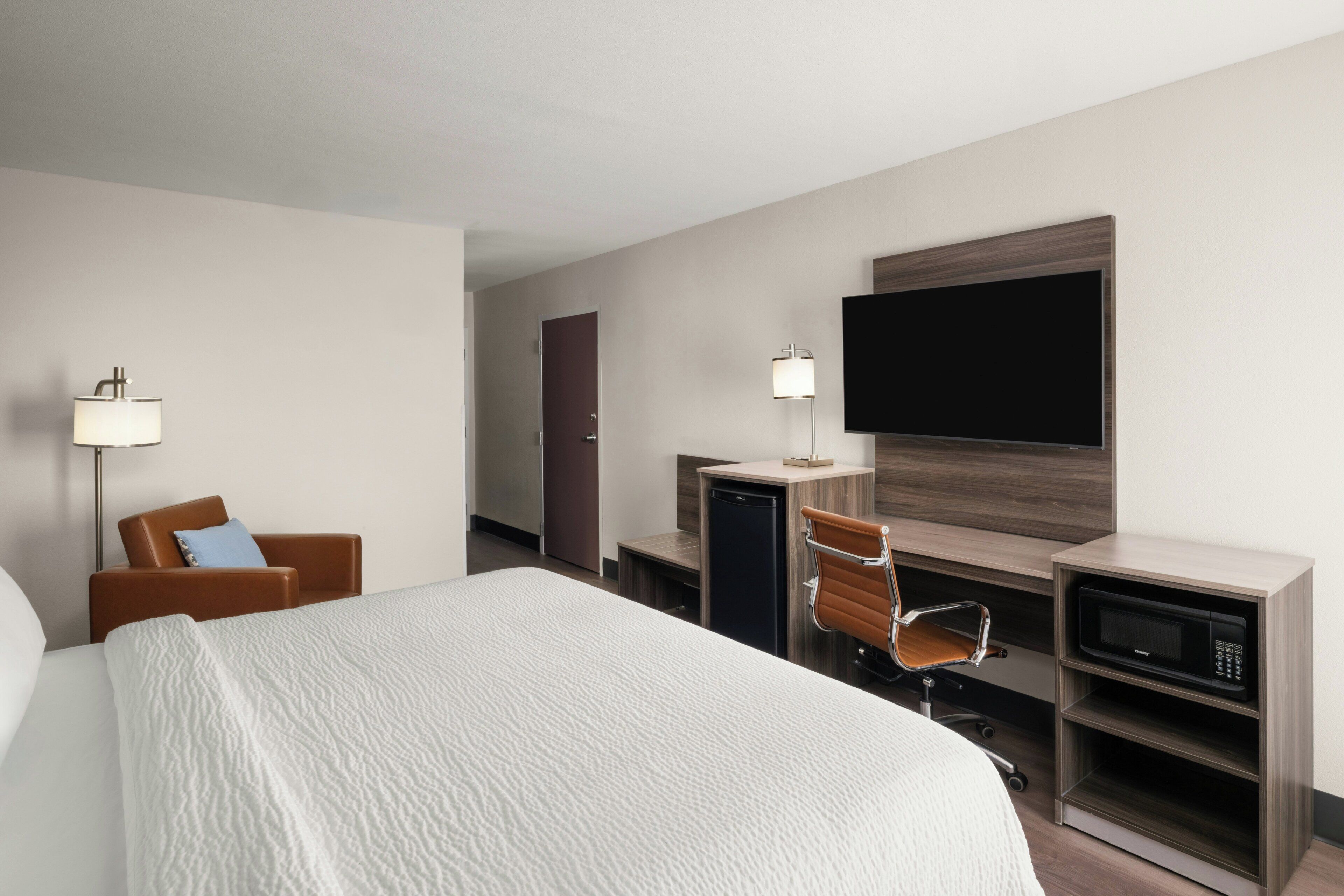 A hotel room with a bed, a desk with a computer, a chair, a television, and a microwave.