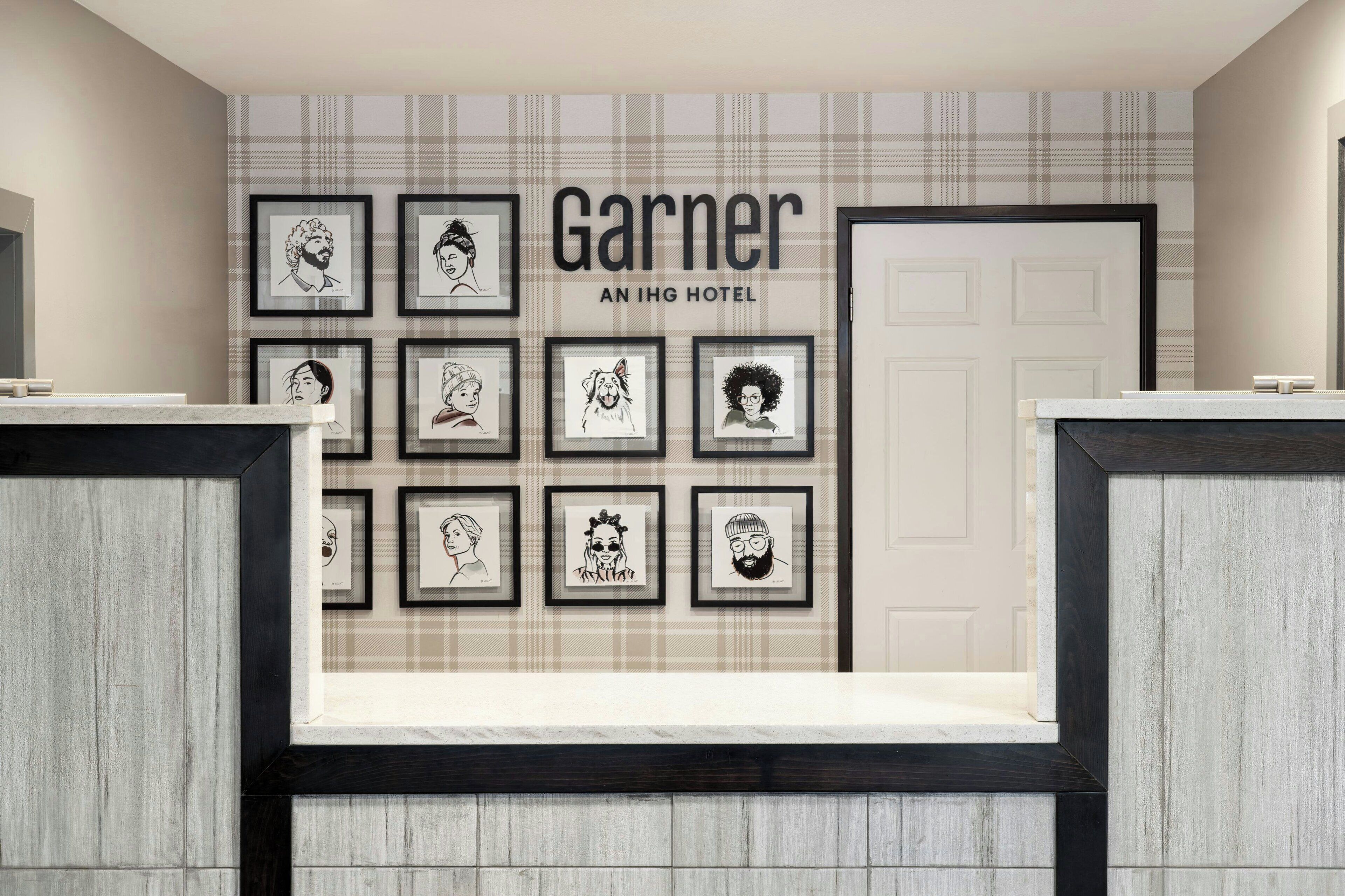 Zona de recepción de un hotel con un cartel en la pared que dice 'Garnier AN IHG HOTEL' y una serie de retratos enmarcados sobre un mostrador de recepción.