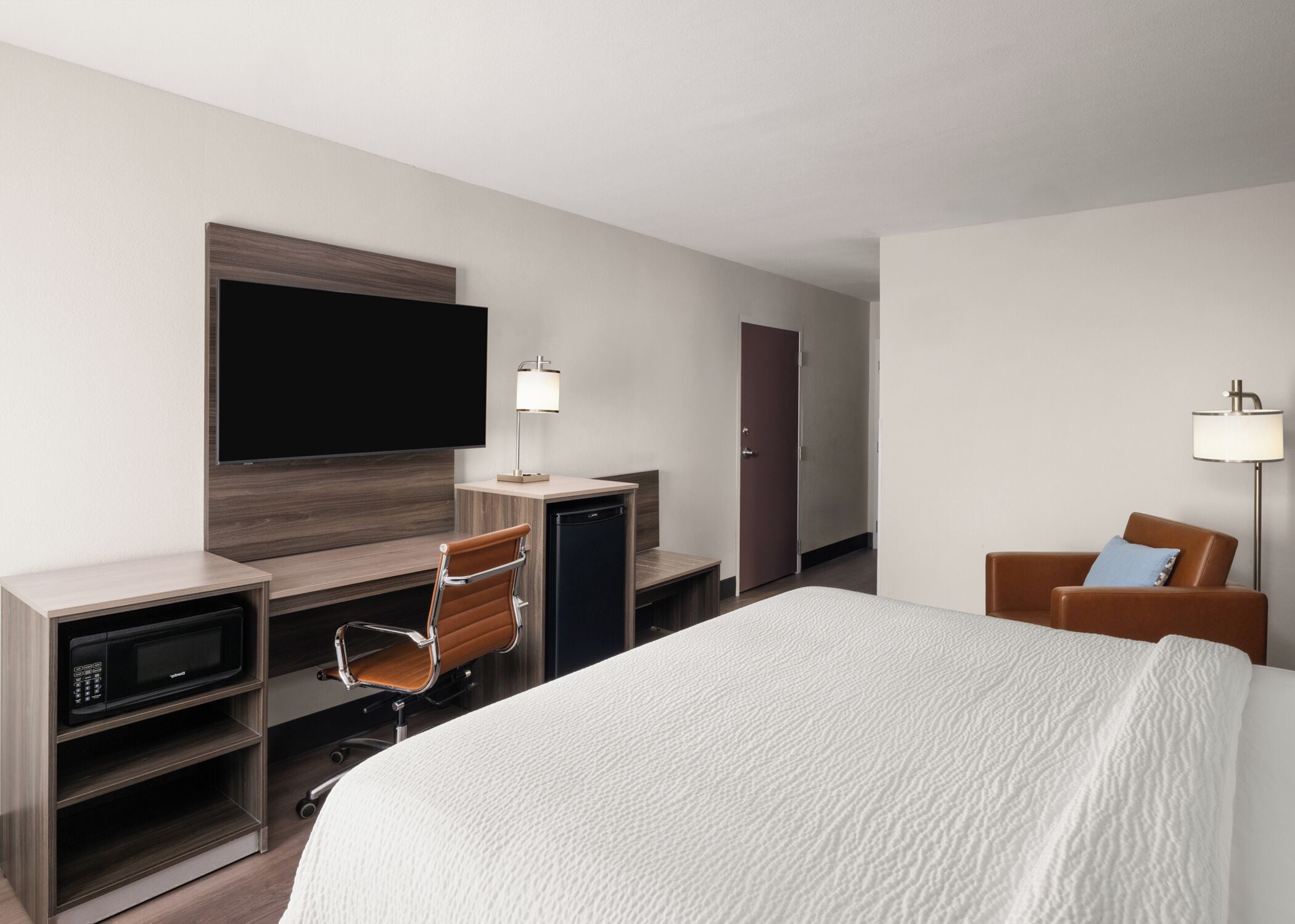 Ein Hotelzimmer mit Bett, Schreibtisch mit Stuhl, Fernseher, Minibar und Kleiderschrank.