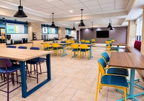 Una cafetería moderna con varias mesas y sillas, una barra con un menú y una pantalla de televisión.