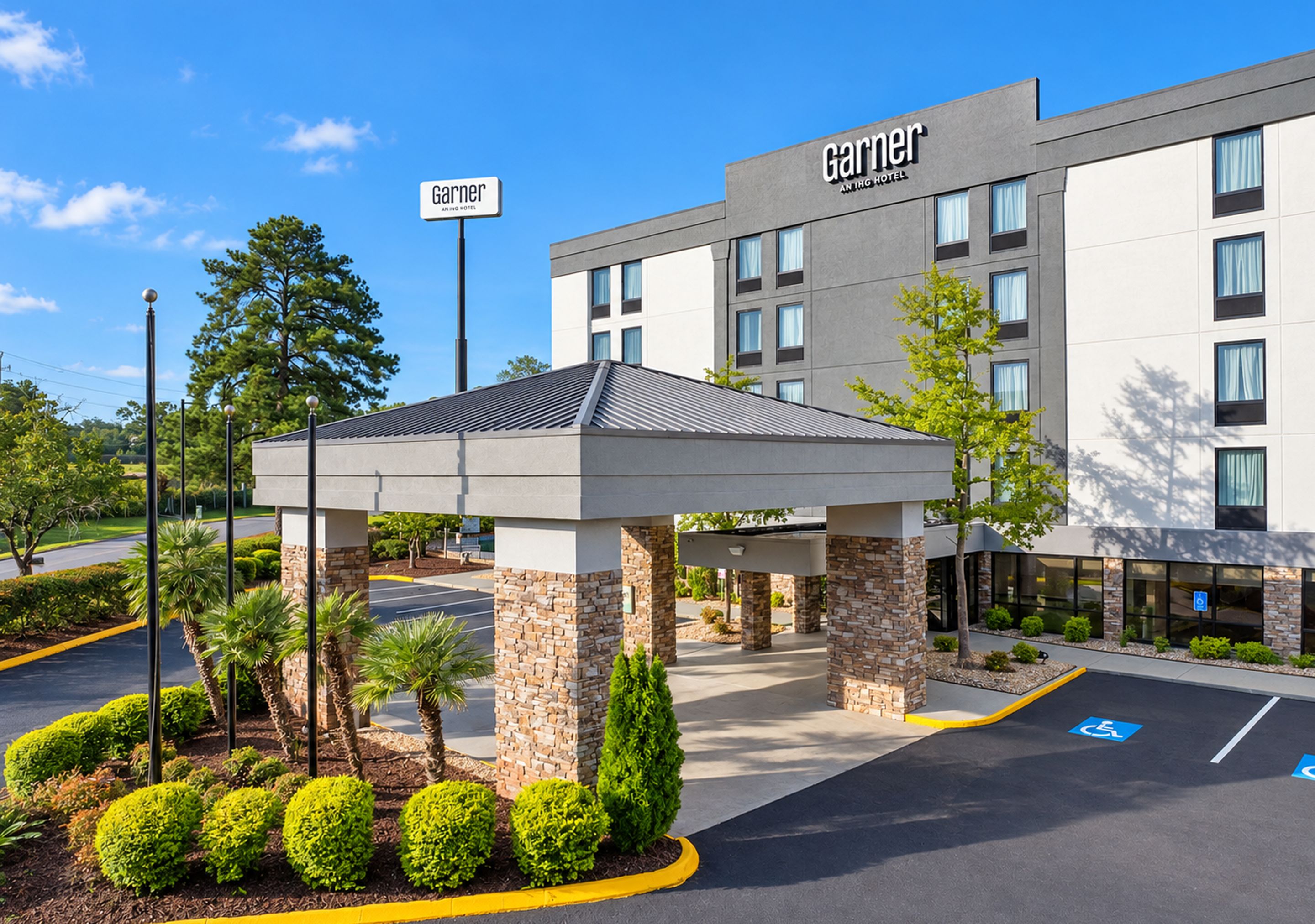 A hotel entrance with a covered waiting area, a parking lot with handicapped parking, and a clear blue sky.