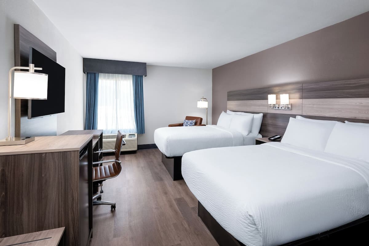 Habitación de hotel con dos camas, un escritorio, una silla, un televisor y una ventana con cortinas.