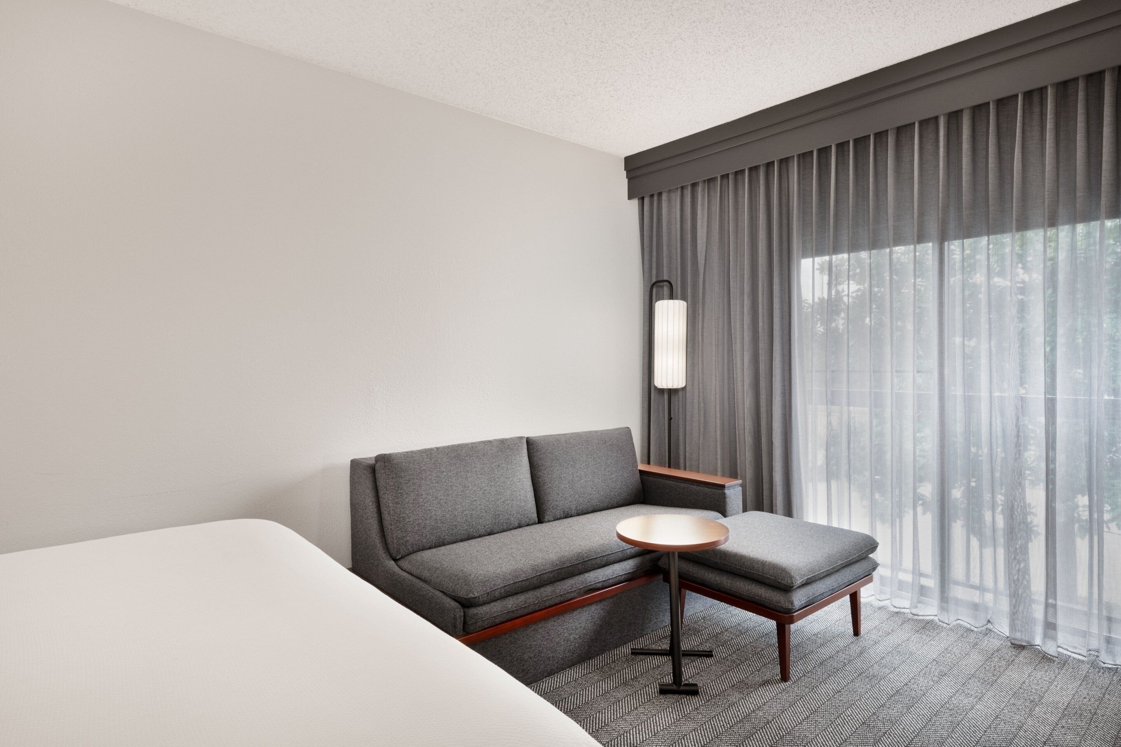 Une chambre d’hôtel avec un canapé gris, une petite table ronde et un lit.