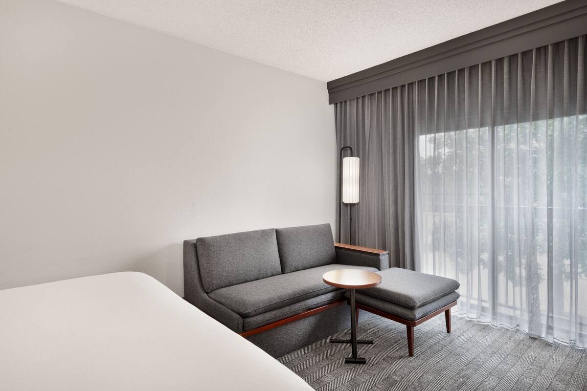 A hotel room with a grey sofa, a small round table, and a bed.