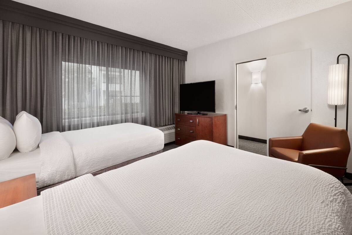 A hotel room with two beds, a television, a dresser, a chair, and a door.