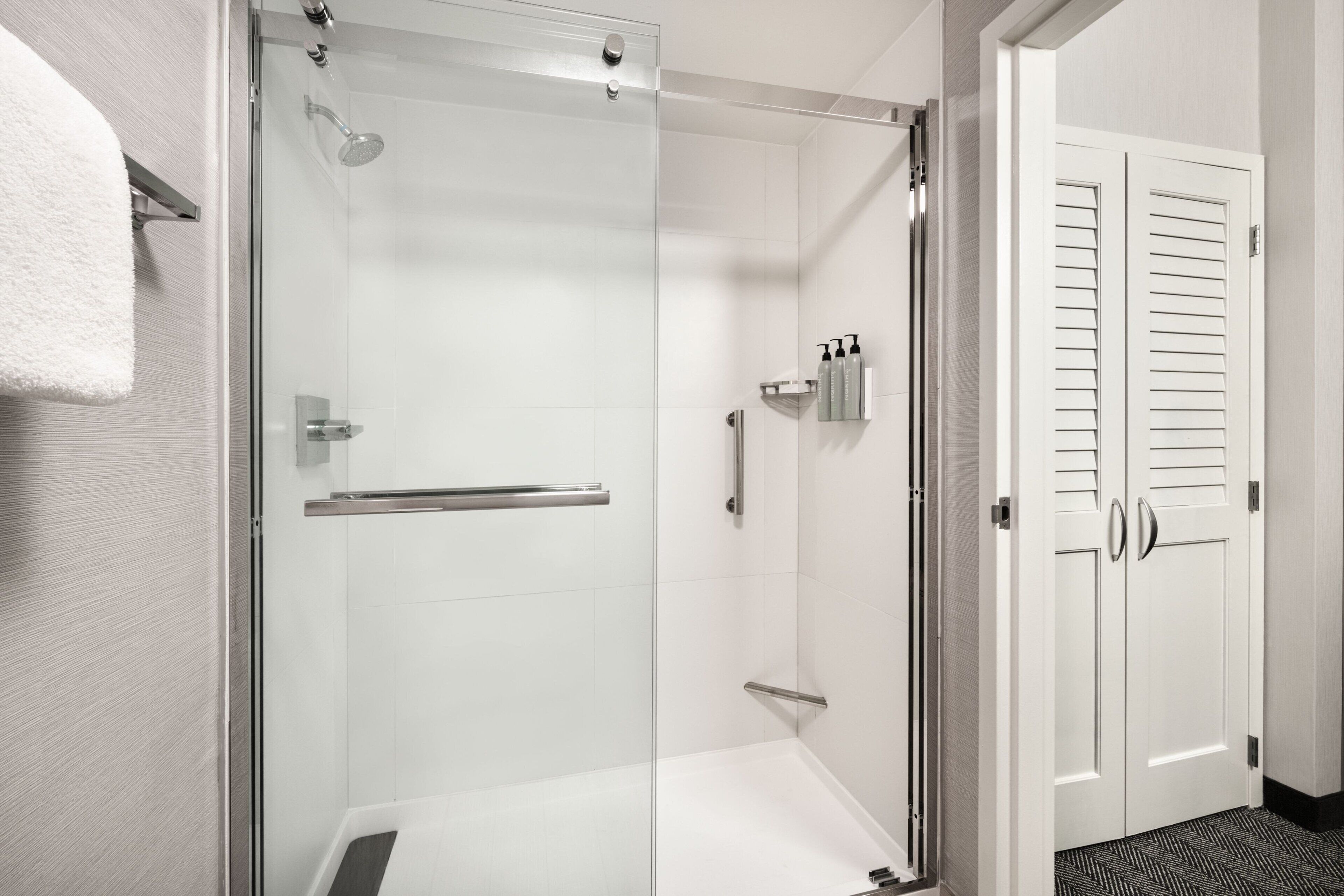 A modern bathroom with a glass-enclosed shower, white tiled walls, and a white door with louvered panels.