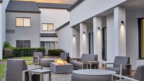 Un espacio de patio con mobiliario exterior, una chimenea y un edificio moderno al fondo.