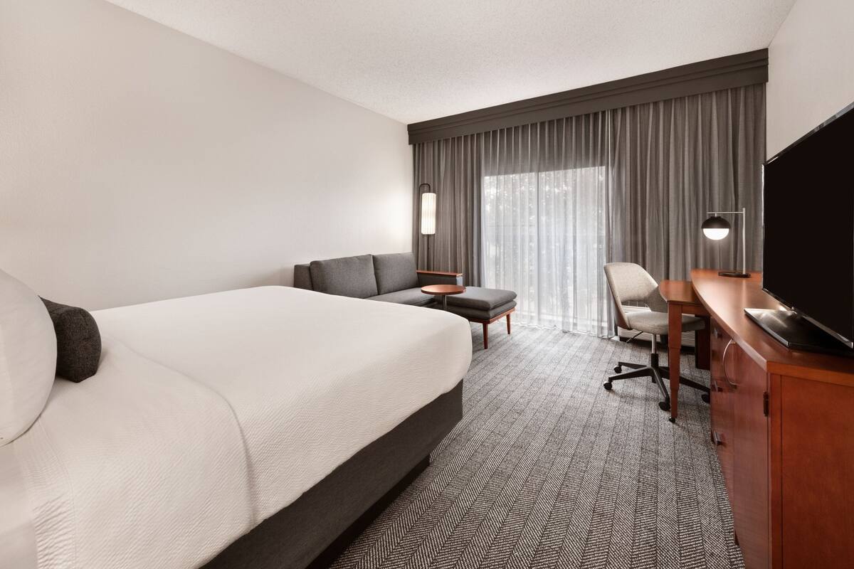 A hotel room with a large bed, a desk, a chair, a television, and a window with curtains.