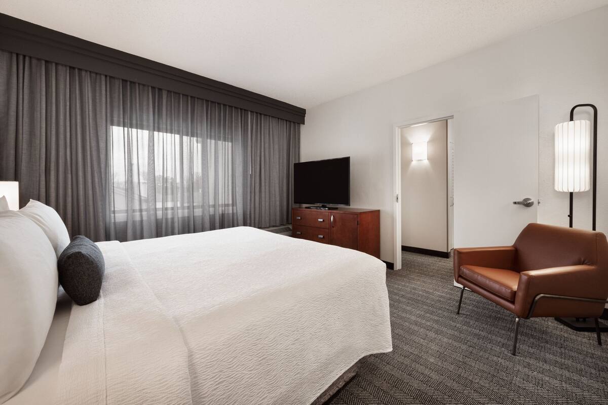 A hotel room with a large bed, a TV, a dresser, a chair, and a lamp.