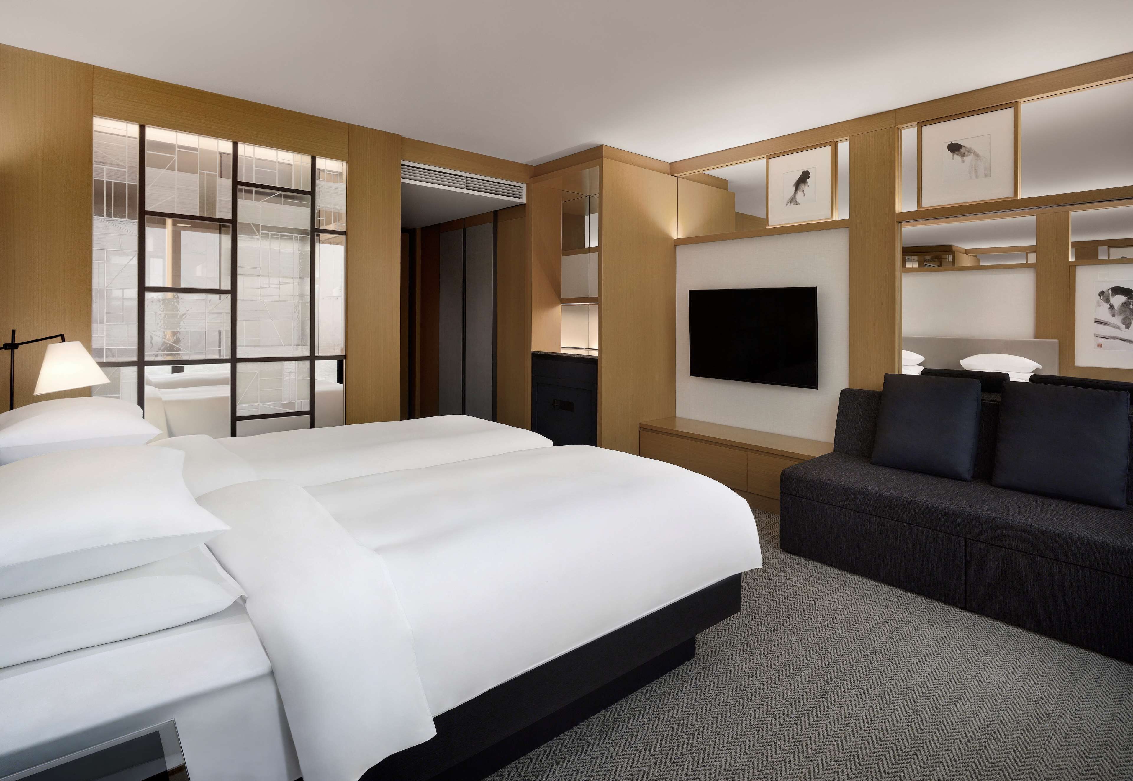 Quarto de hotel com uma cama grande, um sofá, uma TV de tela plana e obras de arte nas paredes.