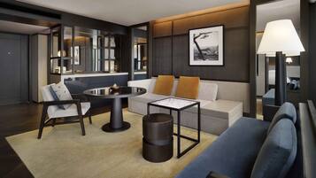Una habitación de hotel moderna con una mesa redonda de comedor, un sofá con cojines naranja, una mesita auxiliar y un espejo grande que refleja la habitación.