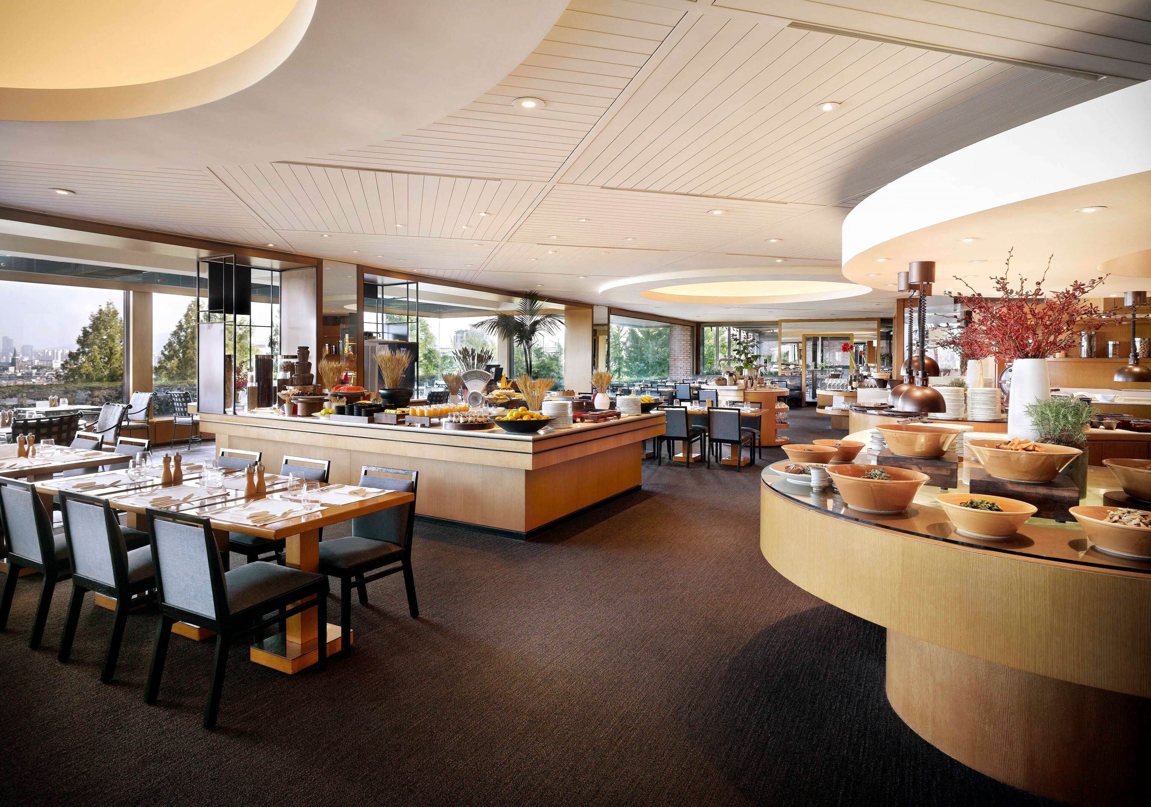 A modern hotel lobby with a central island, seating area, and large windows offering a city view.