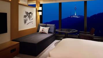 A hotel room with a bed, a small seating area, a table, and a large window with a view of a tower.