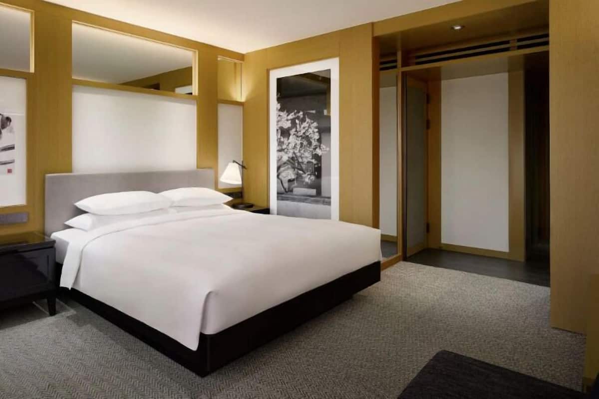 A hotel room with a large bed, a nightstand, a lamp, and a wardrobe.