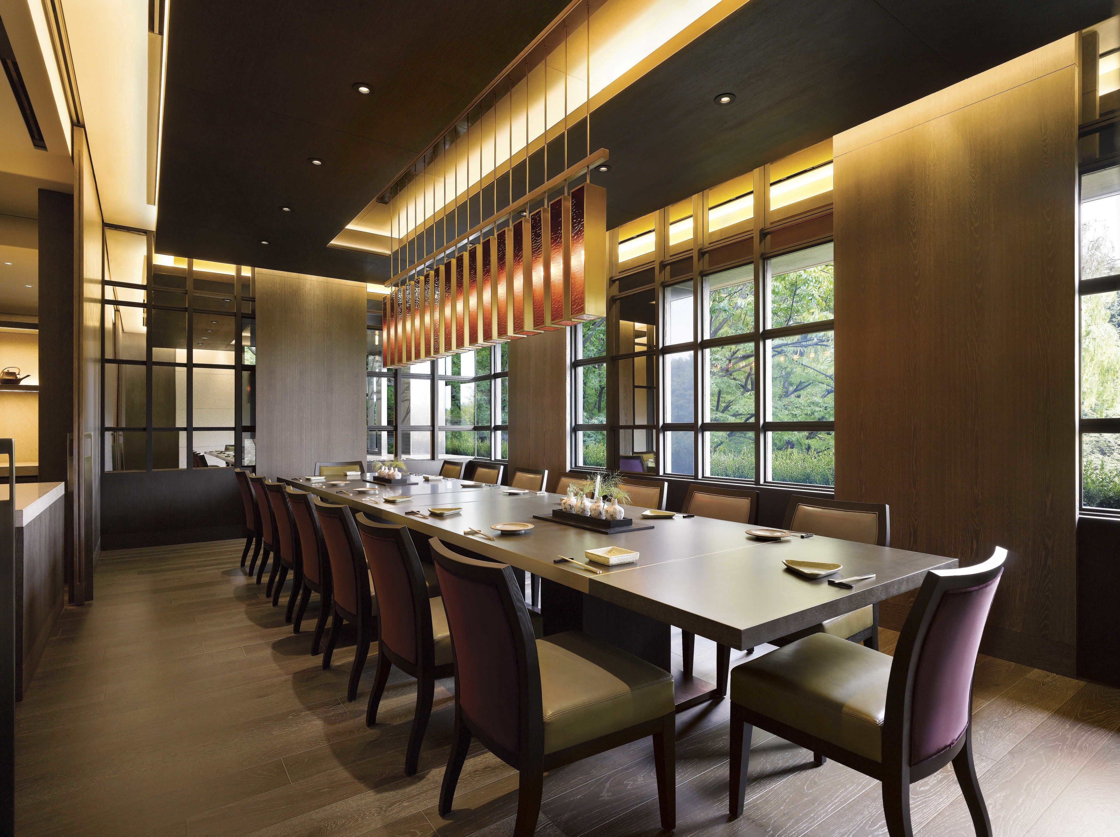 A conference room with a long table, chairs, and large windows with a view of greenery.