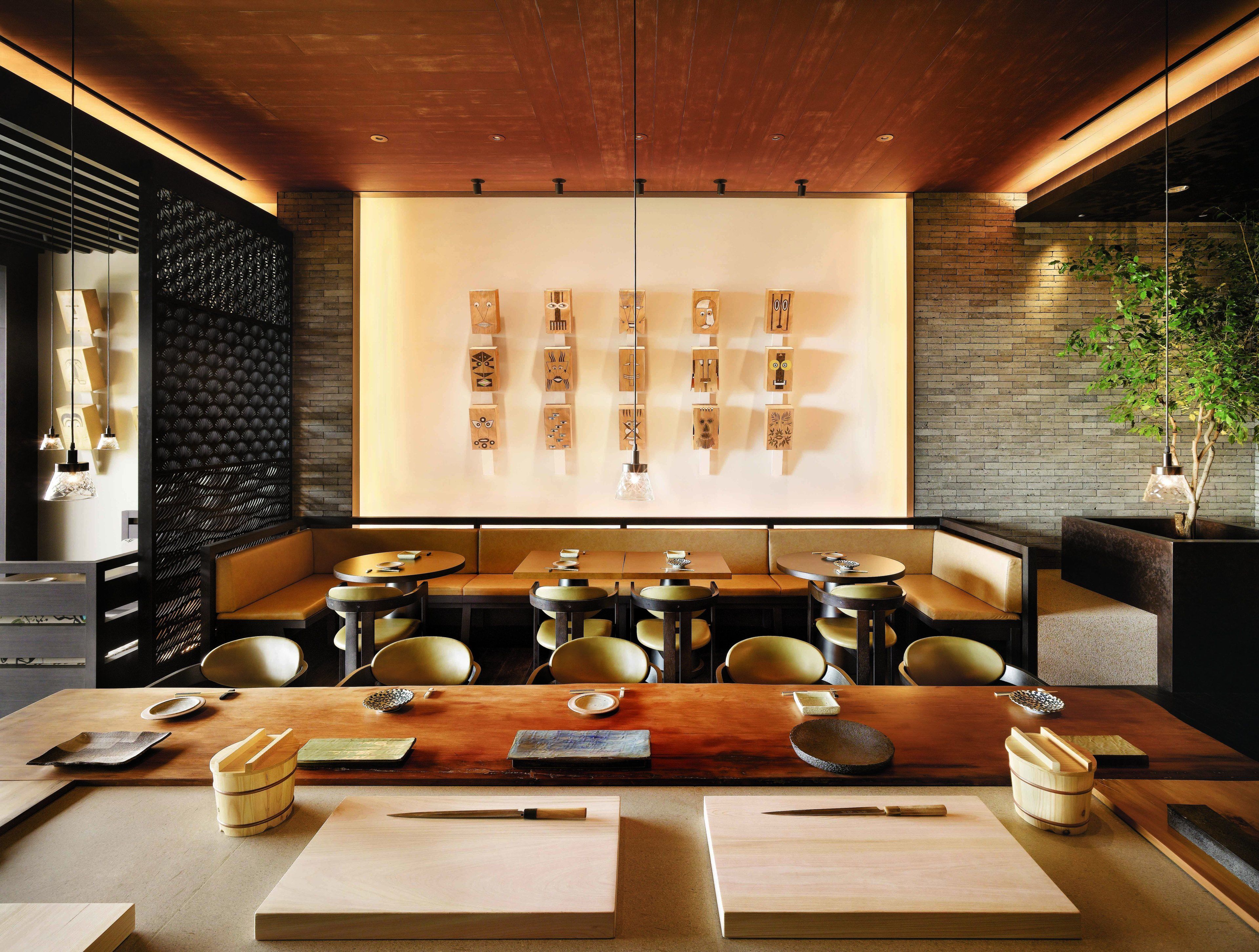 A modern dining area with wooden tables and booths, a brick wall, and a decorative wall with wooden art pieces.