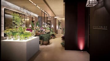A hotel lobby with a reception desk, a variety of potted plants, and a sign for the Steak House.