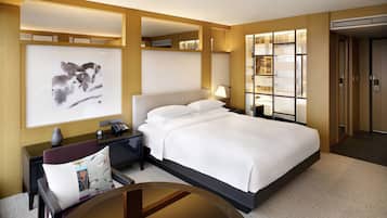 Habitación de hotel con una cama grande, un escritorio con lámpara, una obra de arte en la pared y vistas de la ciudad a través de una ventana.