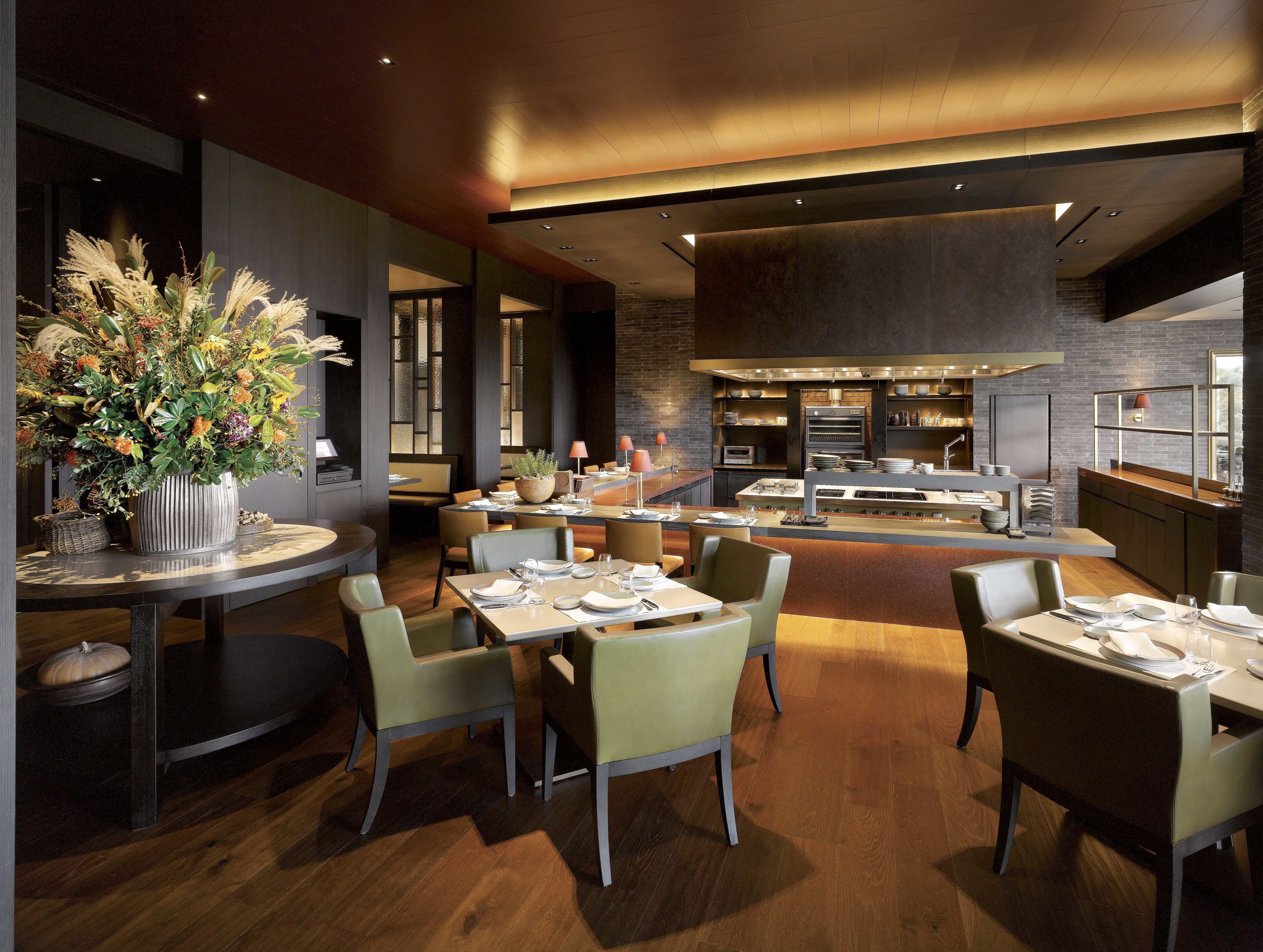 A modern restaurant with a central island, wooden flooring, and a large floral arrangement.