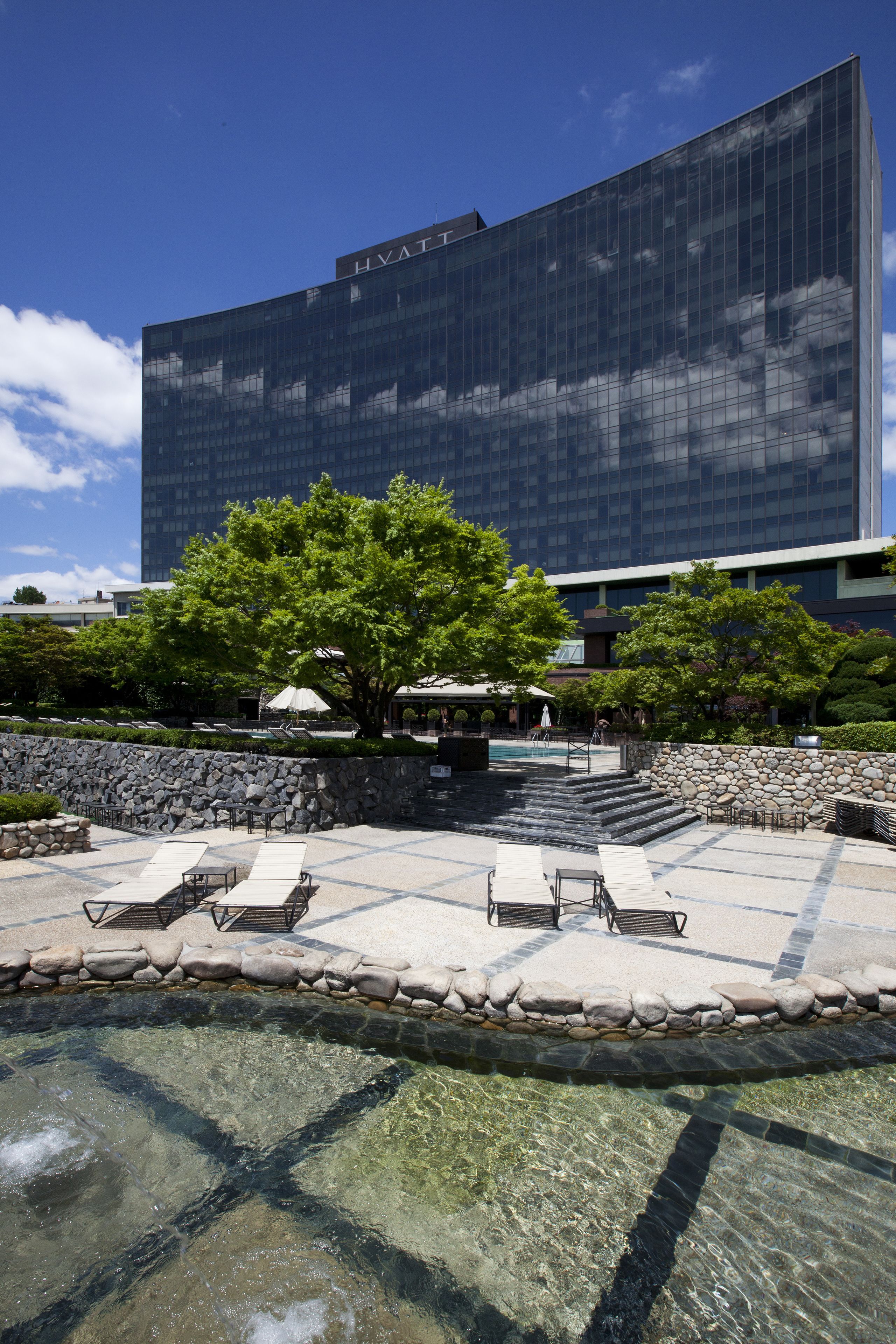 A modern hotel with a swimming pool, lounge chairs, and a stone wall.