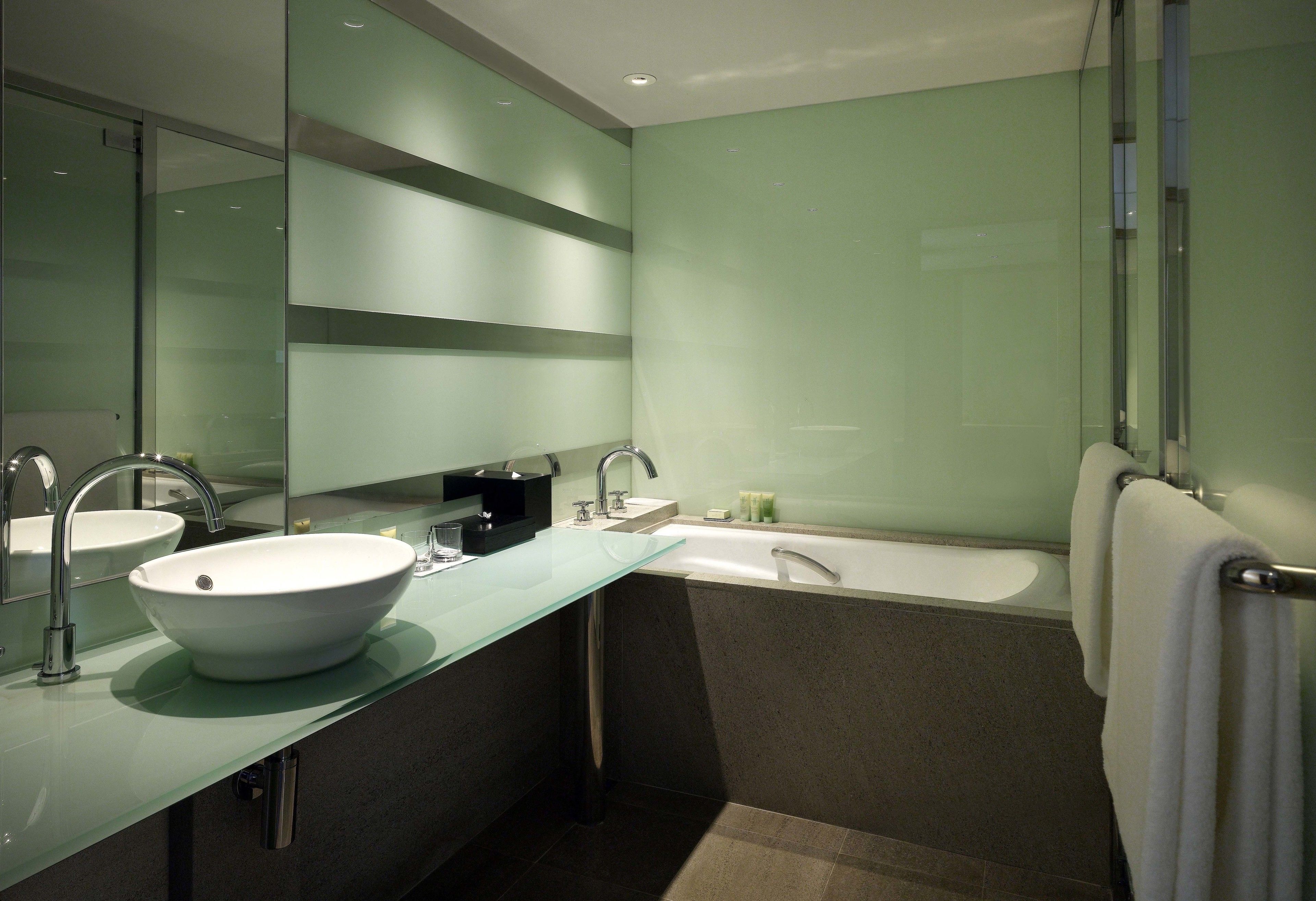 Un baño moderno con un lavabo de vidrio, una bañera y un espejo grande.