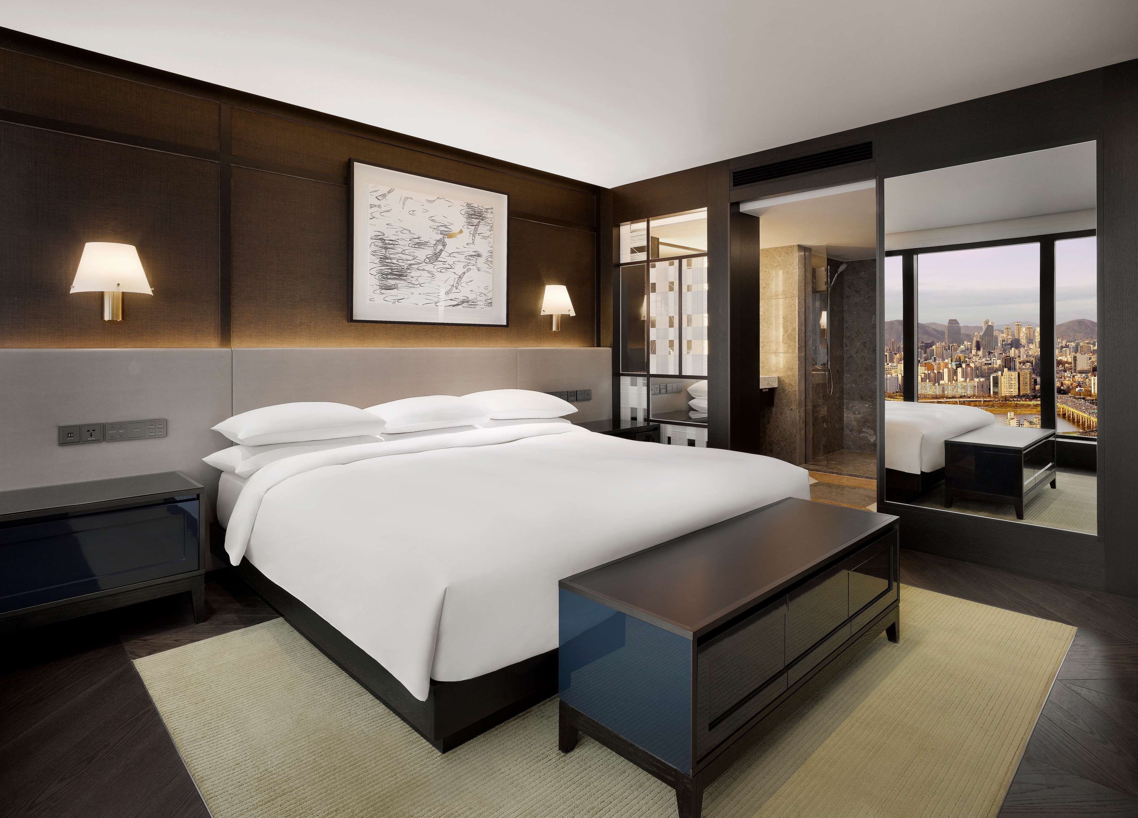 A modern hotel room with a large bed, bedside lamps, a city view, and a glass door leading to a balcony.