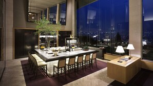 Un comedor moderno con una mesa grande, sillas, un jarrón con flores y vistas de la ciudad de noche.