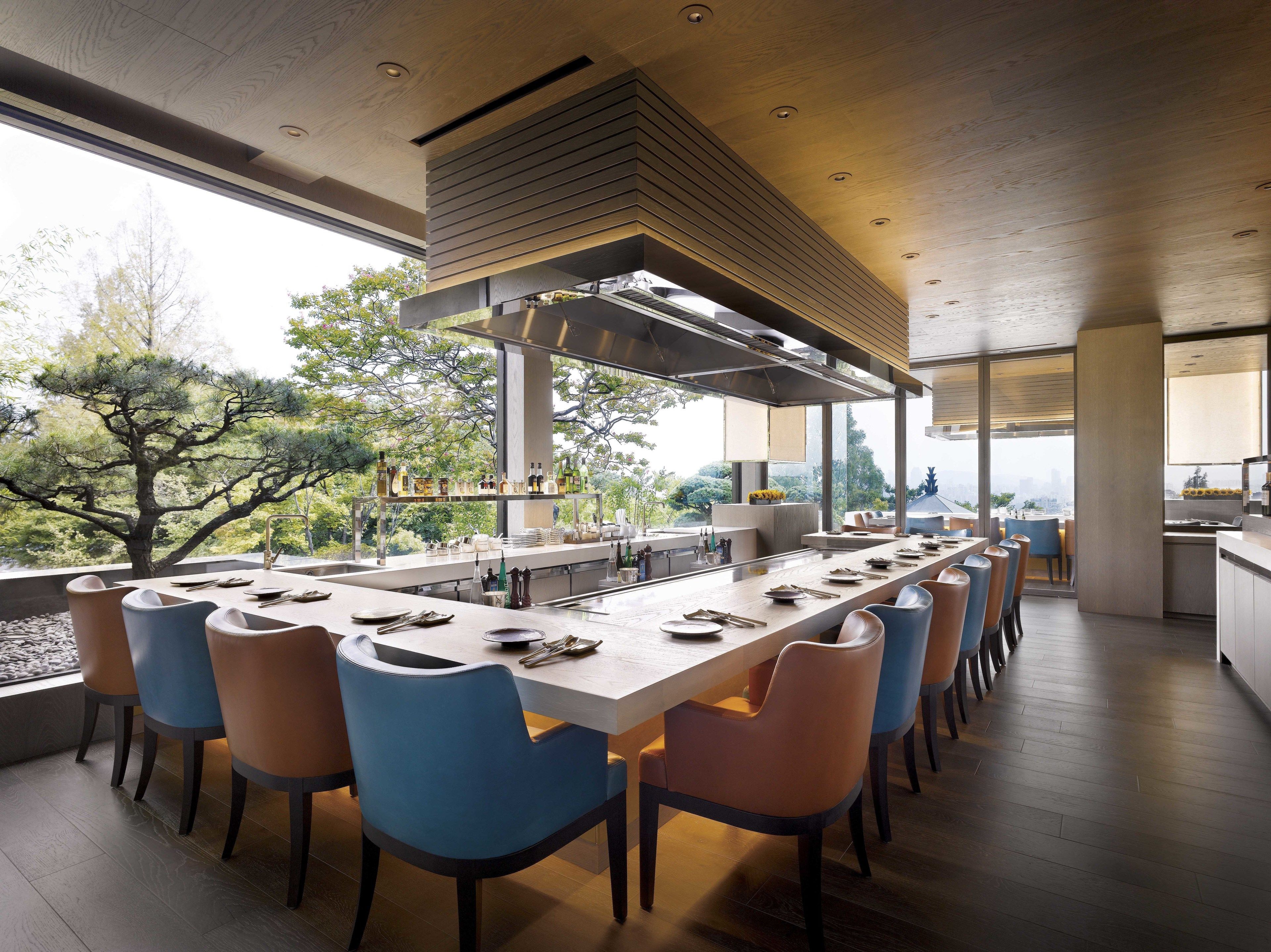 A modern kitchen with a long island, bar seating, and a view of trees.