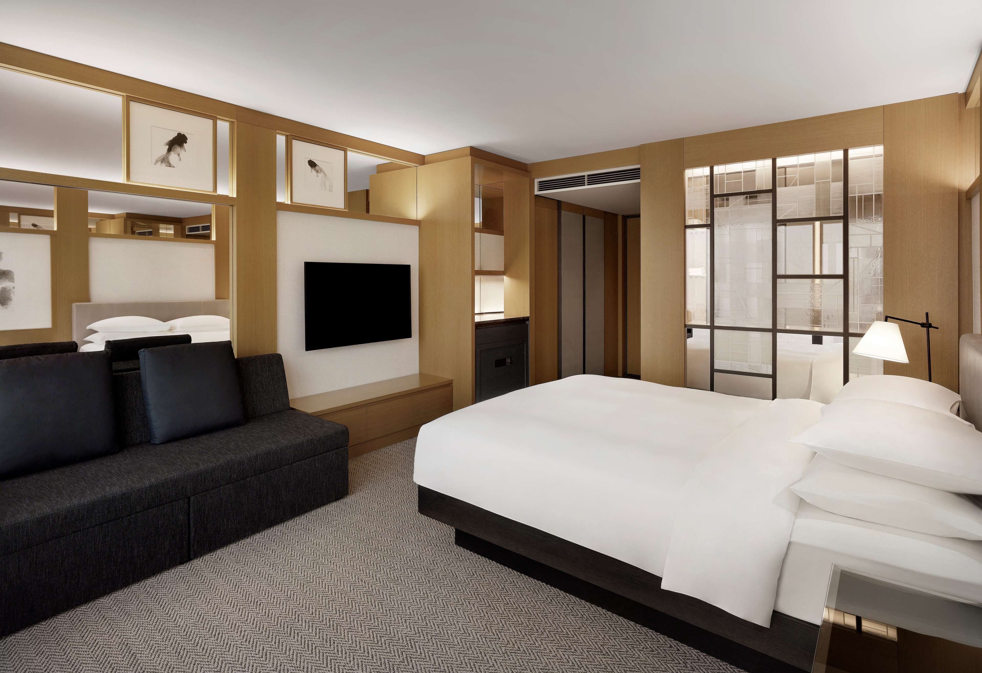 Quarto de hotel moderno com uma cama grande, um sofá, uma televisão de tela plana e quadros nas paredes.