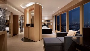 Una habitación de hotel moderna con una cama grande, una zona de estar y vistas de la ciudad de noche.