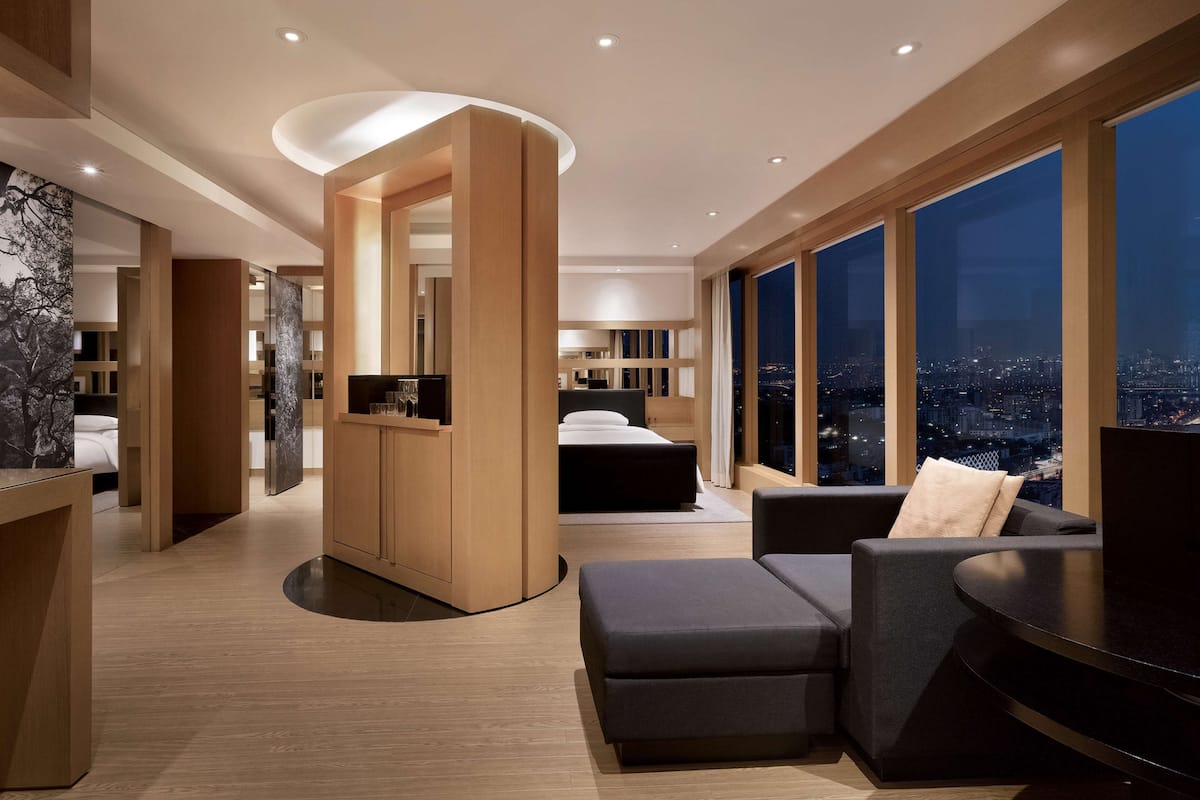 A modern hotel room with a large bed, a seating area, and a view of the city at night.