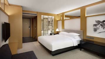A modern hotel room with a large bed, a bedside table with a lamp, a TV mounted on the wall, and a large artwork on the wall.