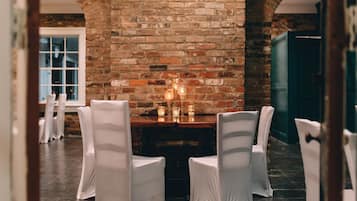 A brick wall with a wooden table and chairs in a room with a tiled floor.