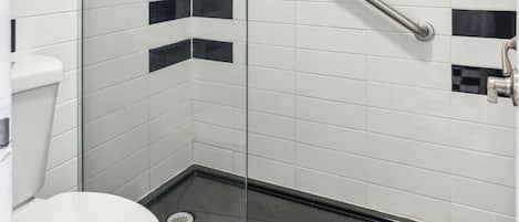A glass-enclosed shower stall with a handheld showerhead, a white toilet, and a black and white tiled wall.