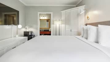Une chambre d’hôtel comprenant un grand lit, une commode avec un miroir, une coiffeuse avec un miroir, une armoire et une table de chevet avec une lampe.