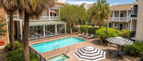 A pool area with lounge chairs, a hot tub, and umbrellas.