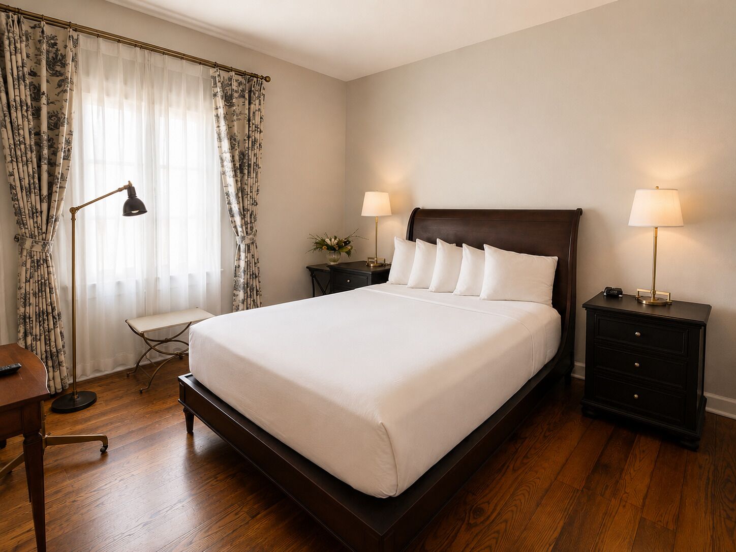 Une chambre à coucher bien rangée, avec un grand lit, deux tables de chevet avec des lampes, un petit bureau et une chaise.