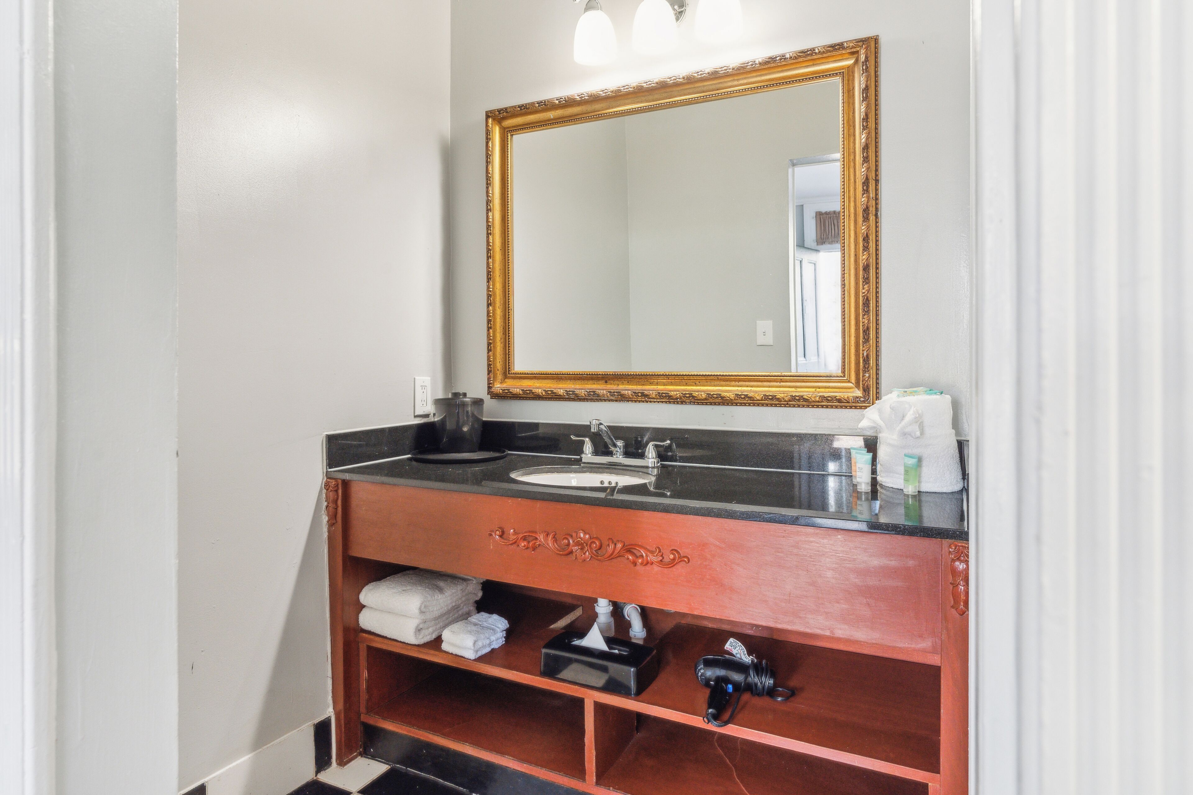 A bathroom with a wooden vanity, a sink, a mirror with a gold frame, and a towel rack.