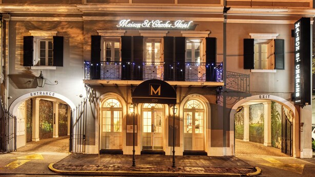 Hotel Maison St. Charles com fachada clássica, uma varanda com luzes de cordão e uma placa de entrada e saída bem visível.