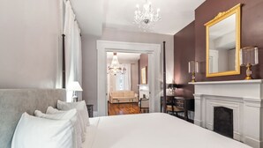 Um quarto espaçoso com uma cama grande, lareira, espelho e um candelabro.