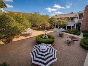 A courtyard with outdoor seating, a fountain, and a building with a balcony. - Maison St Charles (New Orleans)