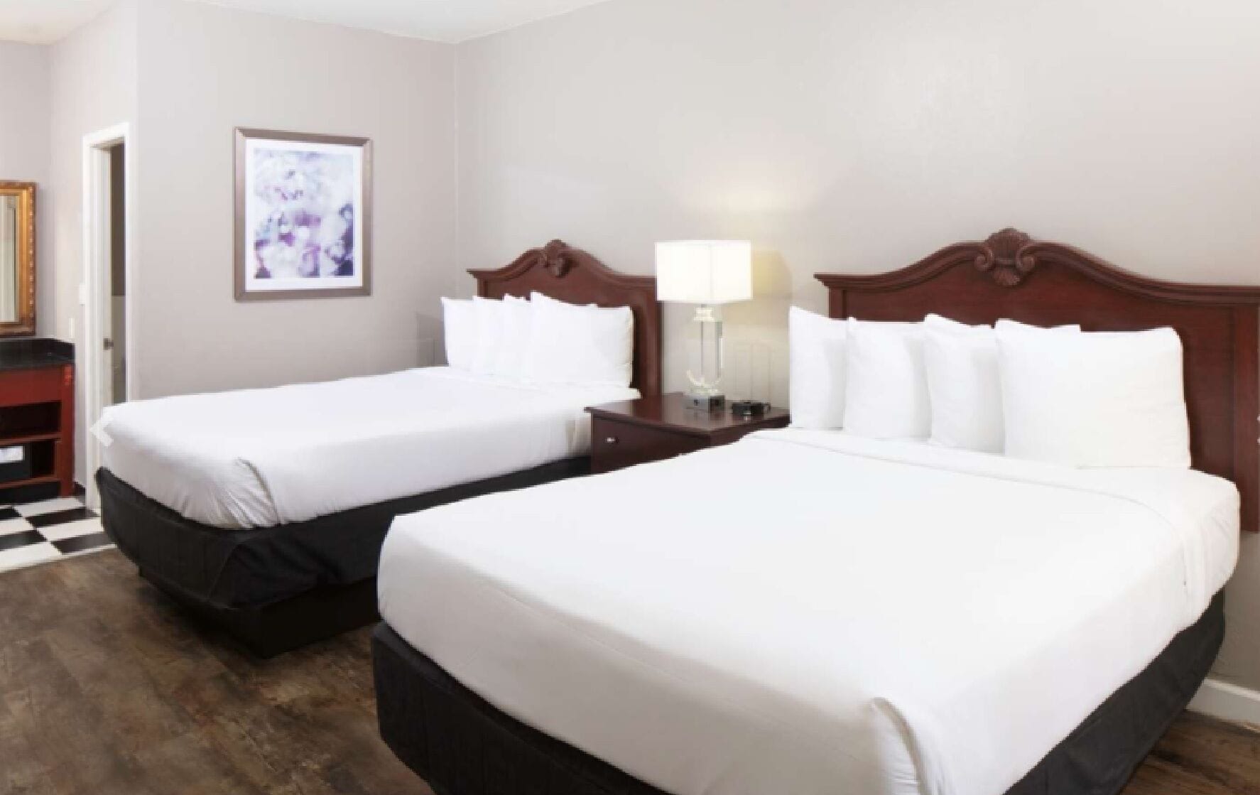 A hotel room with two beds, a nightstand, a lamp, and a framed picture on the wall.
