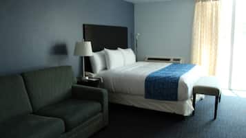A hotel room with a bed, a green sofa, a bedside table with a lamp, and a window with curtains.