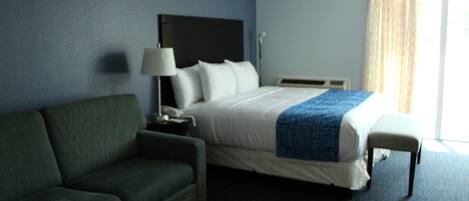 A hotel room with a bed, a green sofa, a bedside table with a lamp, and a window with curtains.