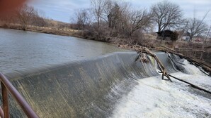 A dam with water flowing over it, surrounded by trees and a clear sky.